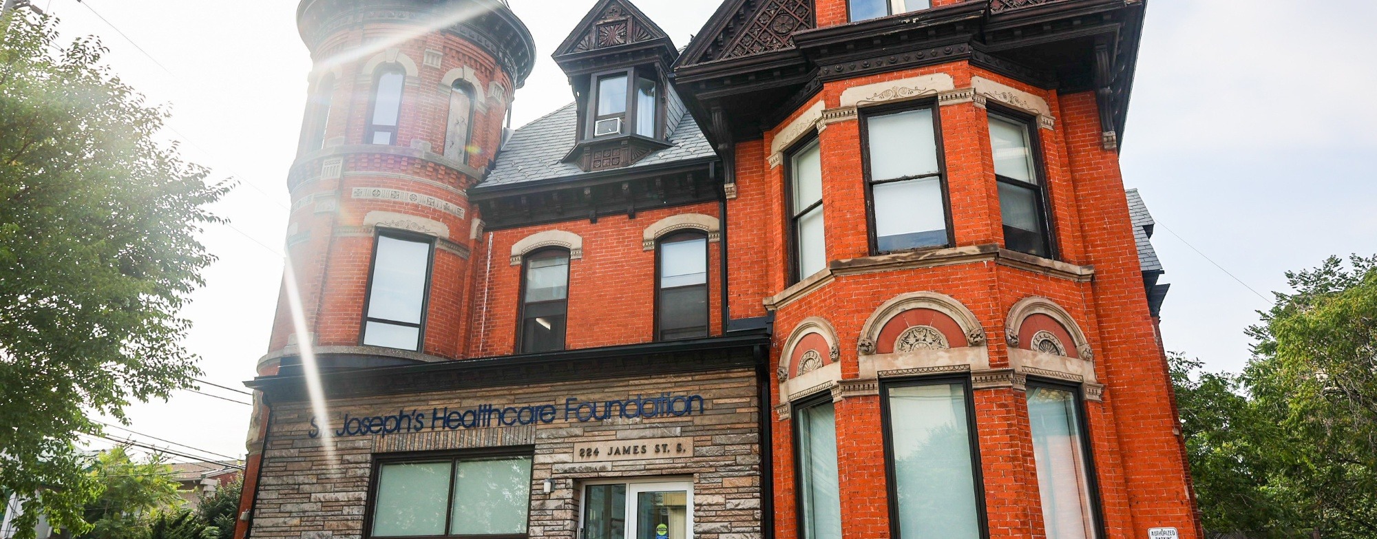 The St. Joseph's Healthcare Foundation building stands tall with the bright sun behind it. It has a bright red brick facade and a dark roof.