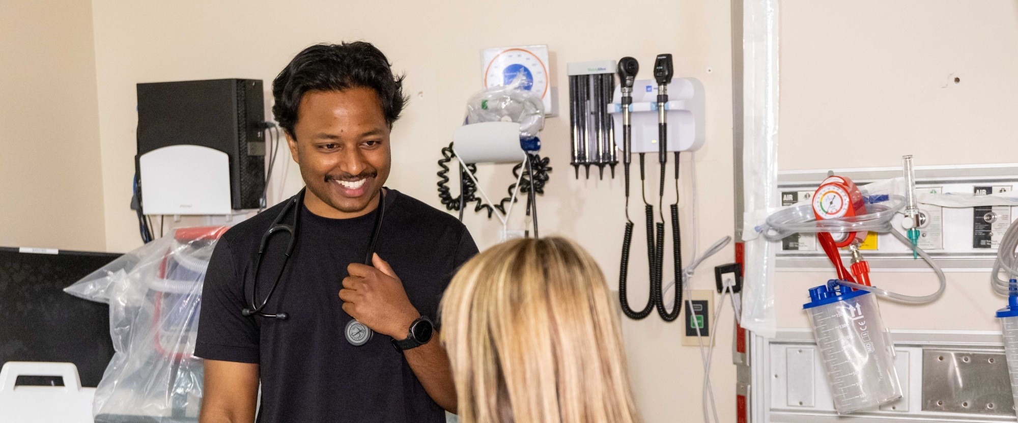 Two people are together in a medical room talking. One stands and smiles, facing the other.