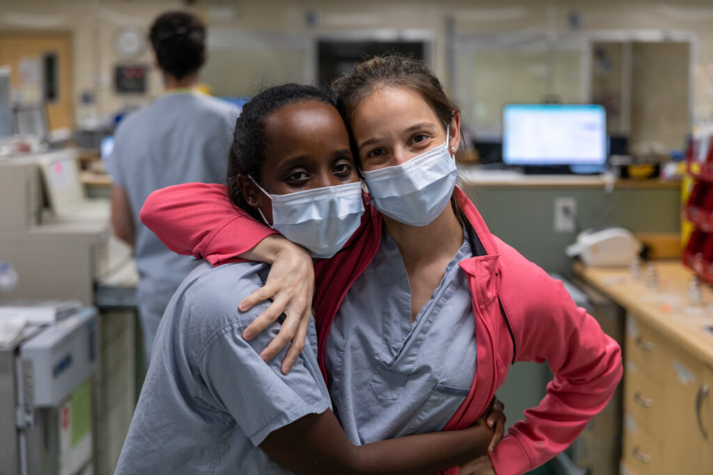 Two girls wearing scrubs and medical masks embrace
